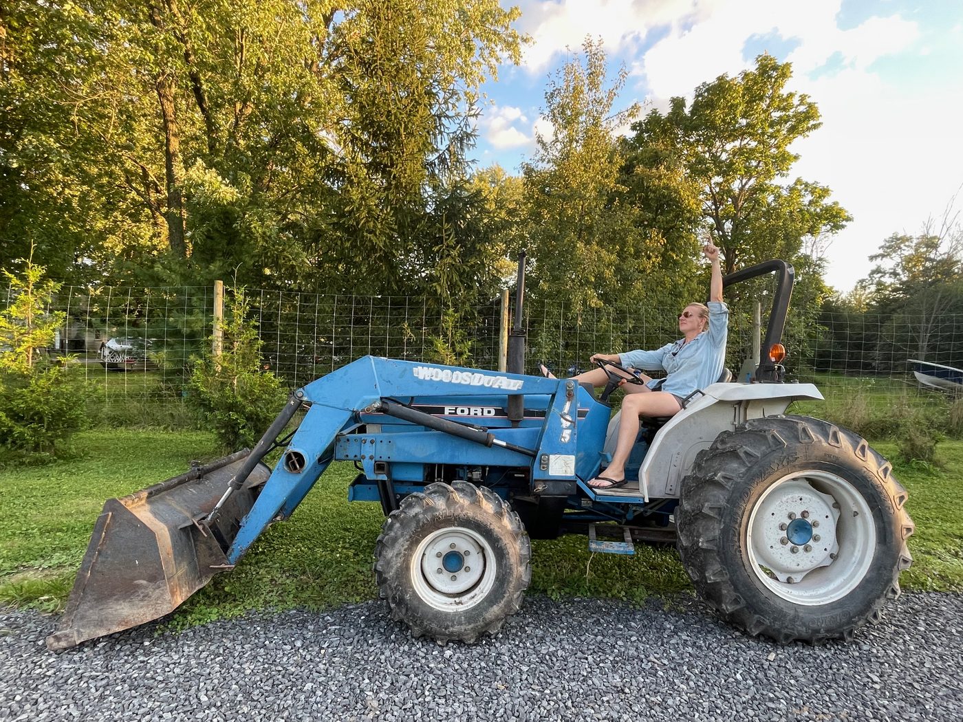 The farmer waving from the seat of a blue Ford tractor.